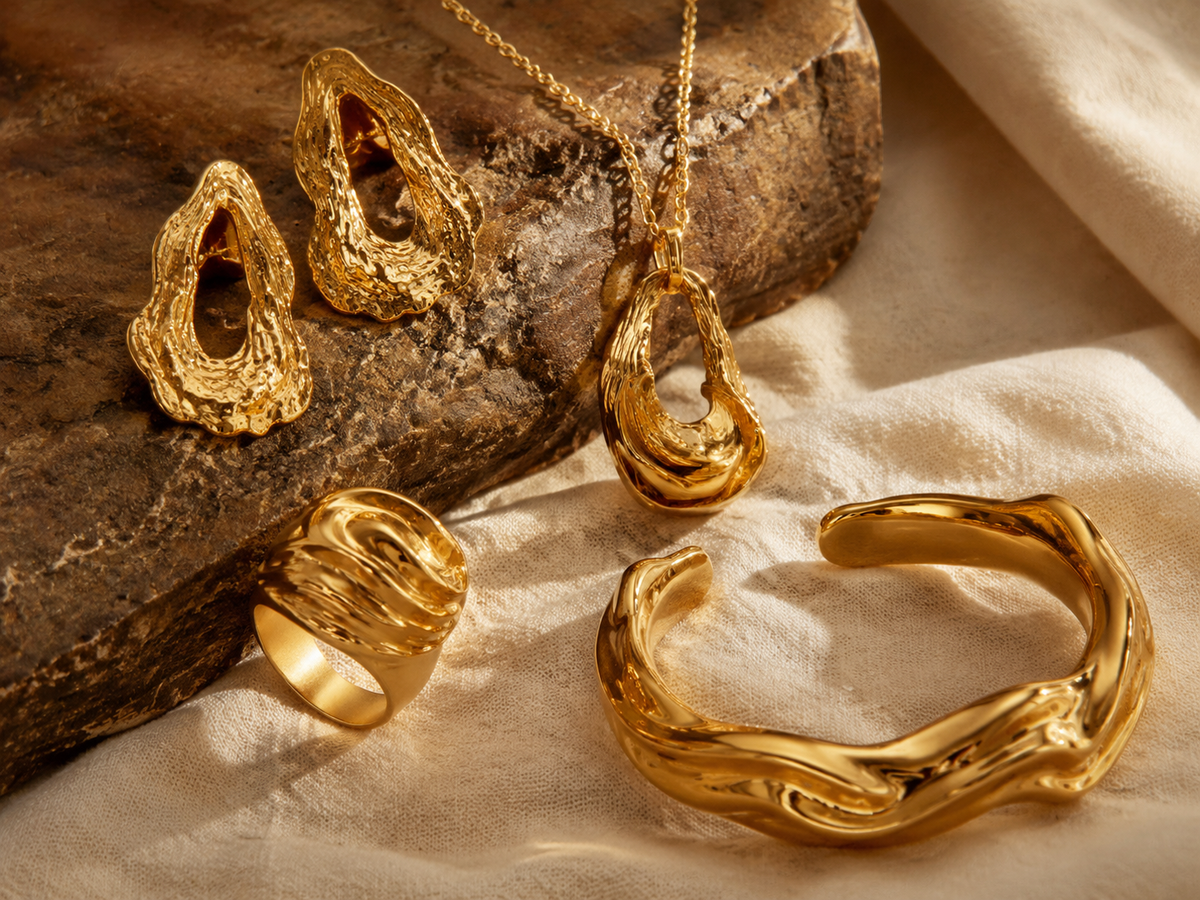 Sculptural gold-plated brass wholesale jewelry collection on brown stone and cream fabric