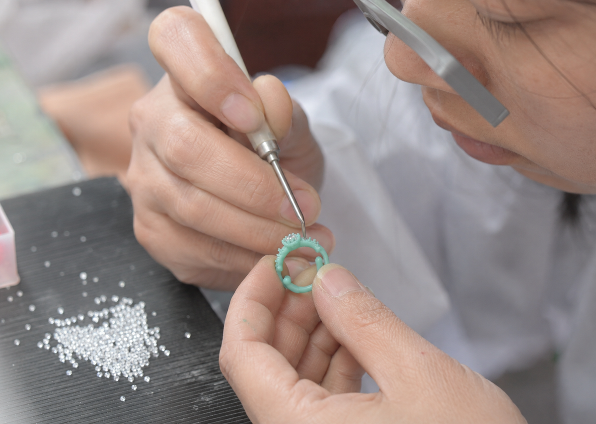 Chinese jewelry technician placing stones into a wax ring model before custom jewelry casting