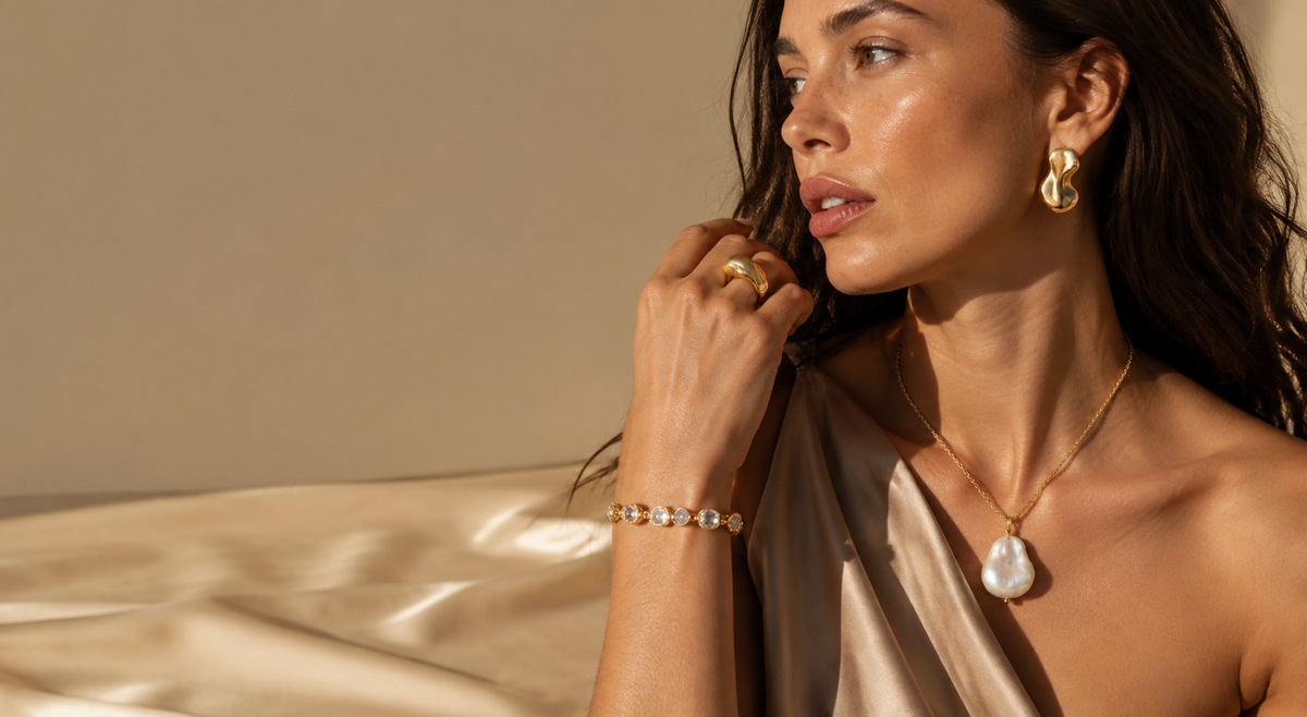 Model wearing sculptural gold-plated brass earrings, baroque pearl pendant necklace, cubic zirconia bracelet and organic gold ring